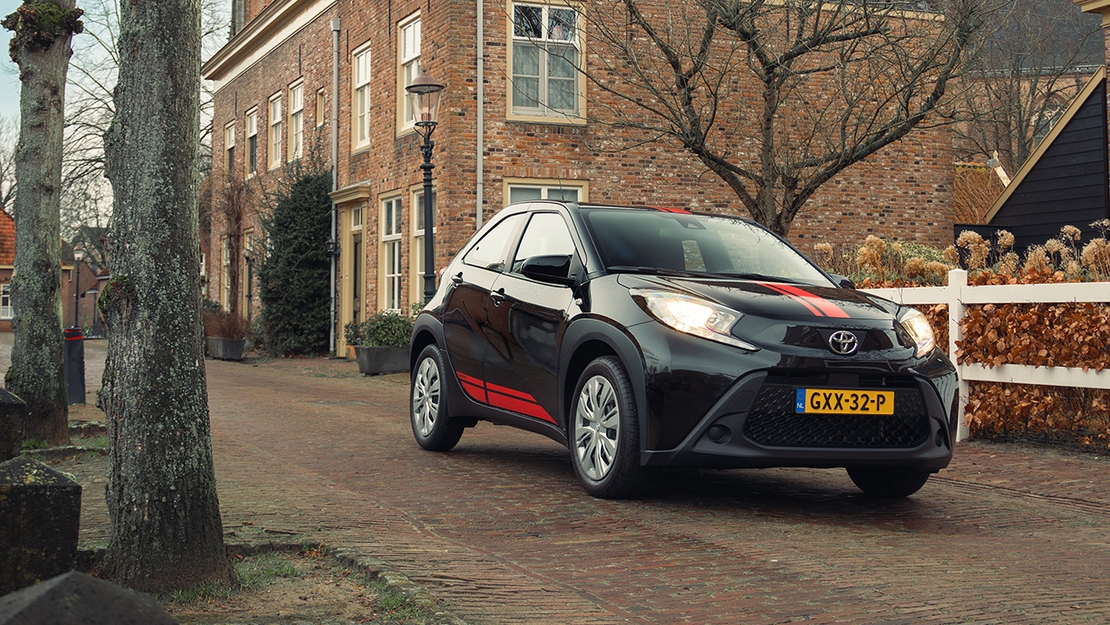 Toyota-Aygo-X-exterieur-driekwart-voor-zwart-rood-met-kerk-op-de-achtergrond